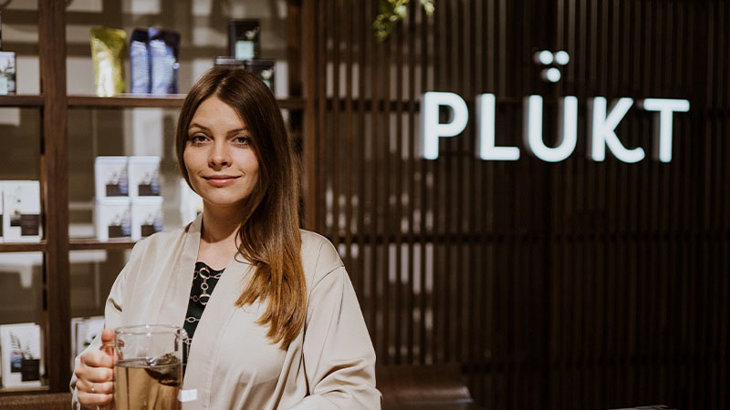 Mara Lieplapa smiling at camera with PLUKT sign in background